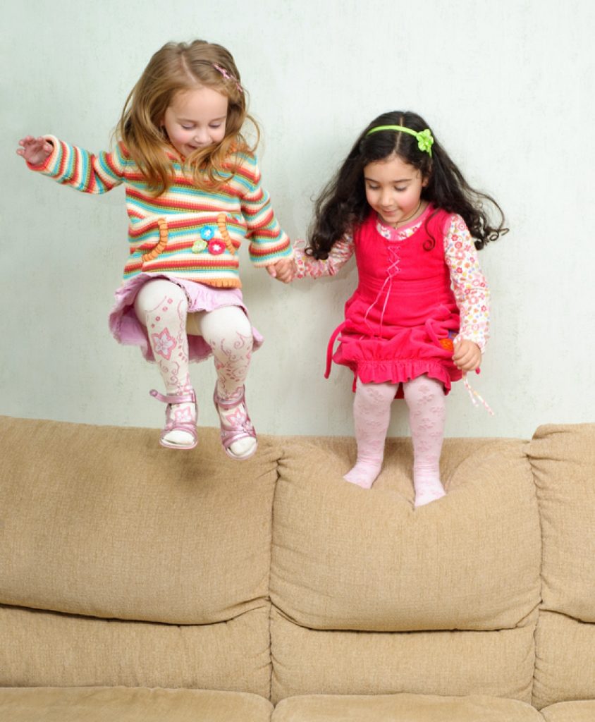 Two little girls jumping on the couch