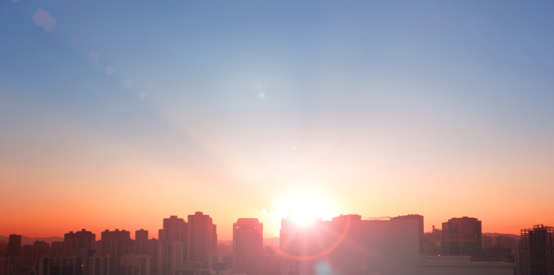 The sun rising over buildings in a city.